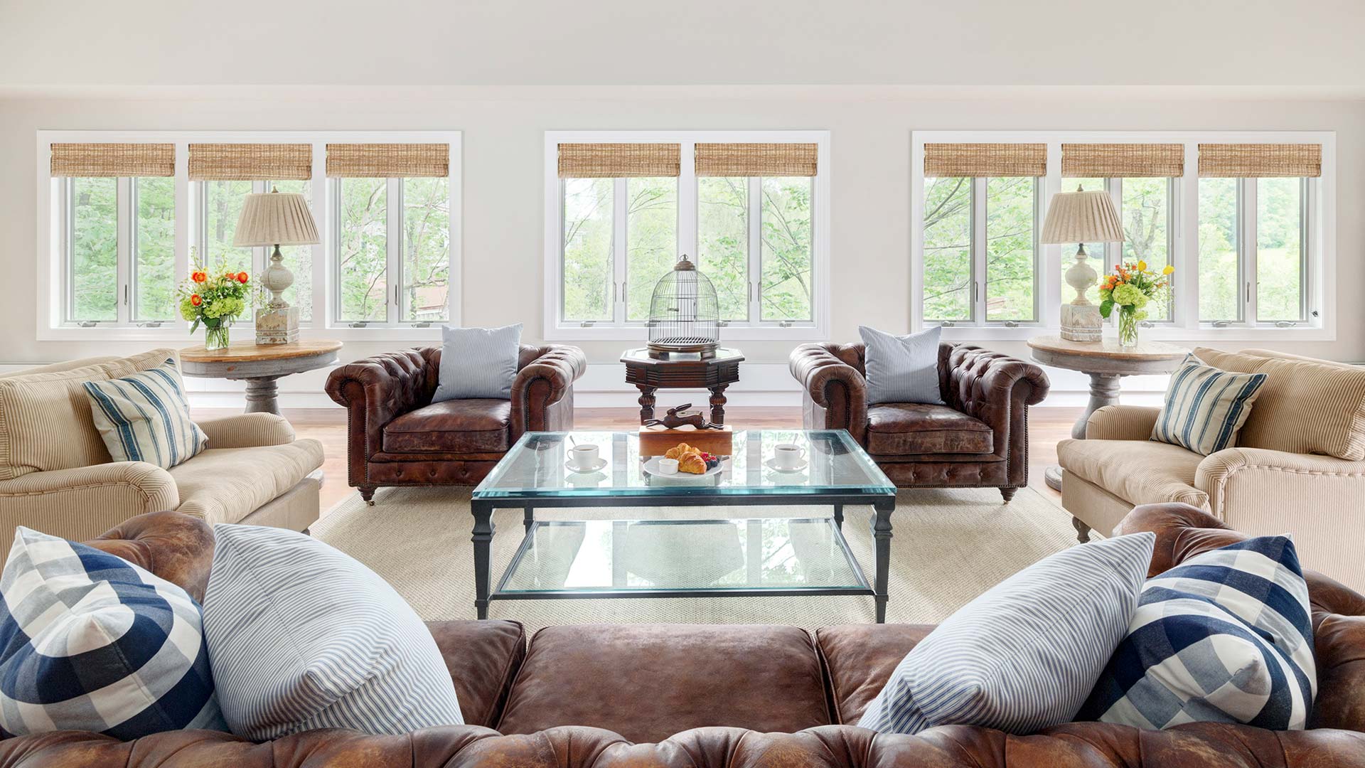interior shot garshak's living area. There is a couch in the foreground and two plush arm chairs on either side of a glass coffee table in front of the couch. There are windows exposing the trees outside.