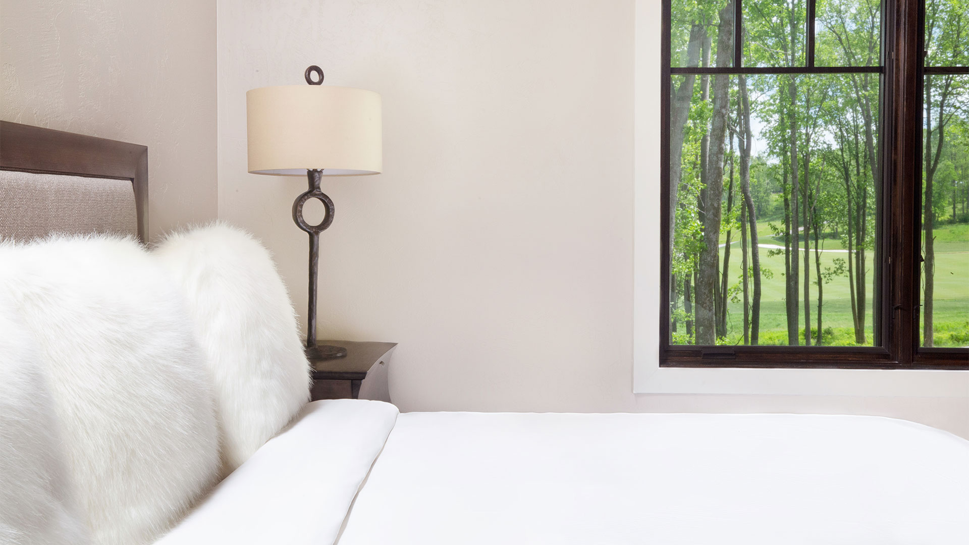detail shot of a dogwood bedroom. There is a elegant bed with all white linens and a bedside table with a lamp