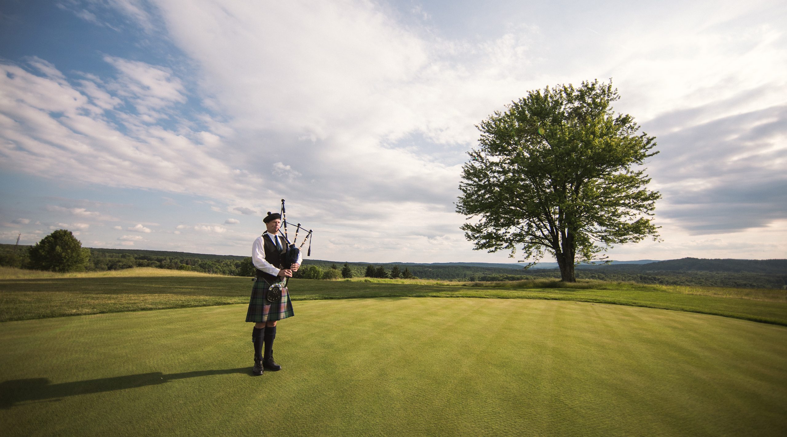 bagpiper on an open field near the lone tree