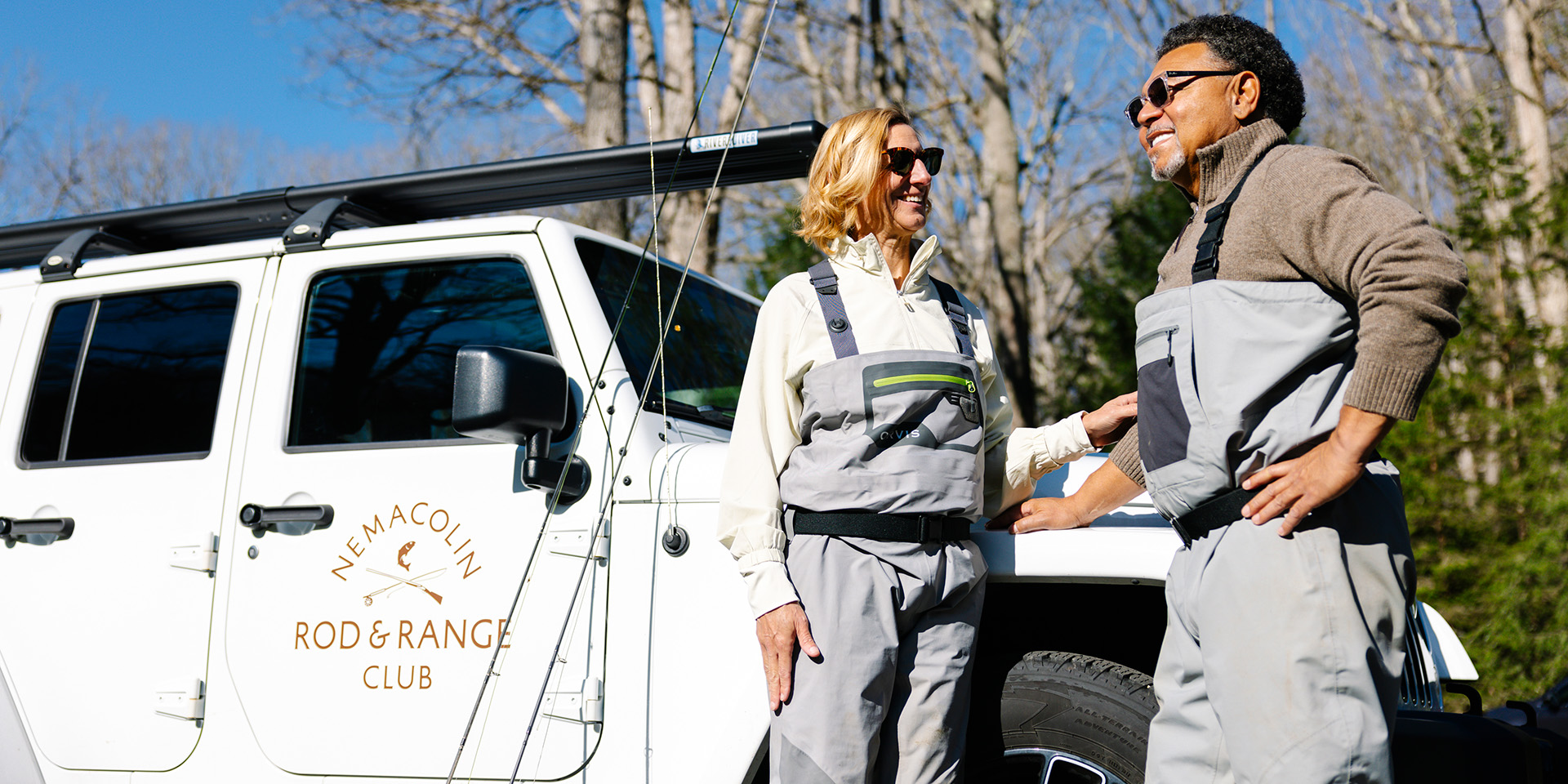 Two people standing against a rod and range logo white jeep