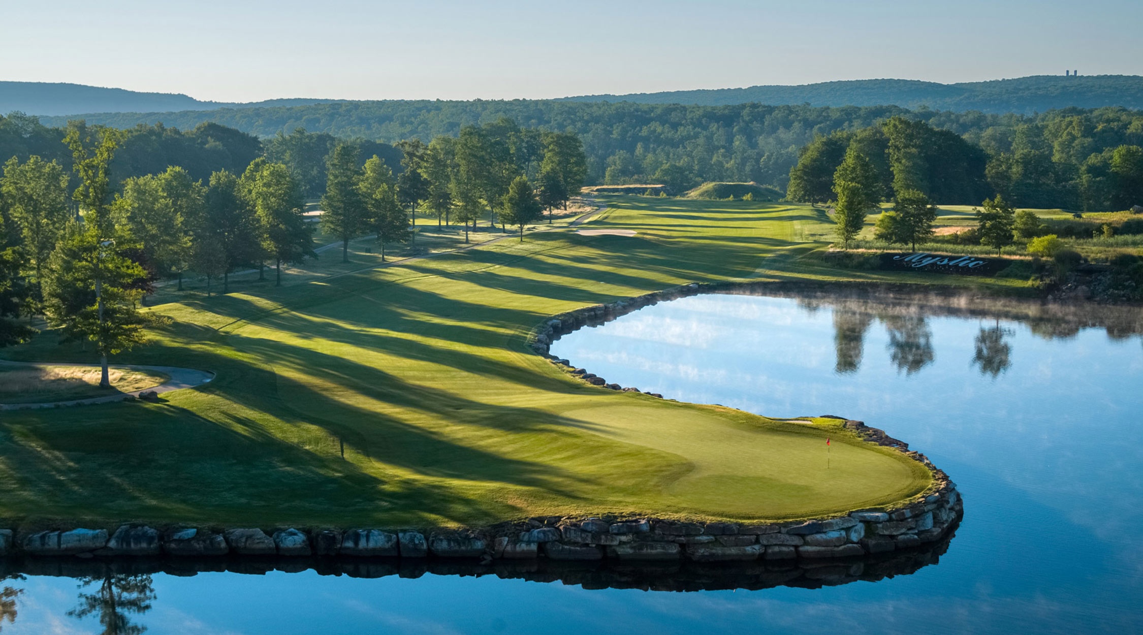 Golf course fairway with mountains in the distance and a pond and water hazzard at the Mystic Rock Golf Course at Nemacolin resort