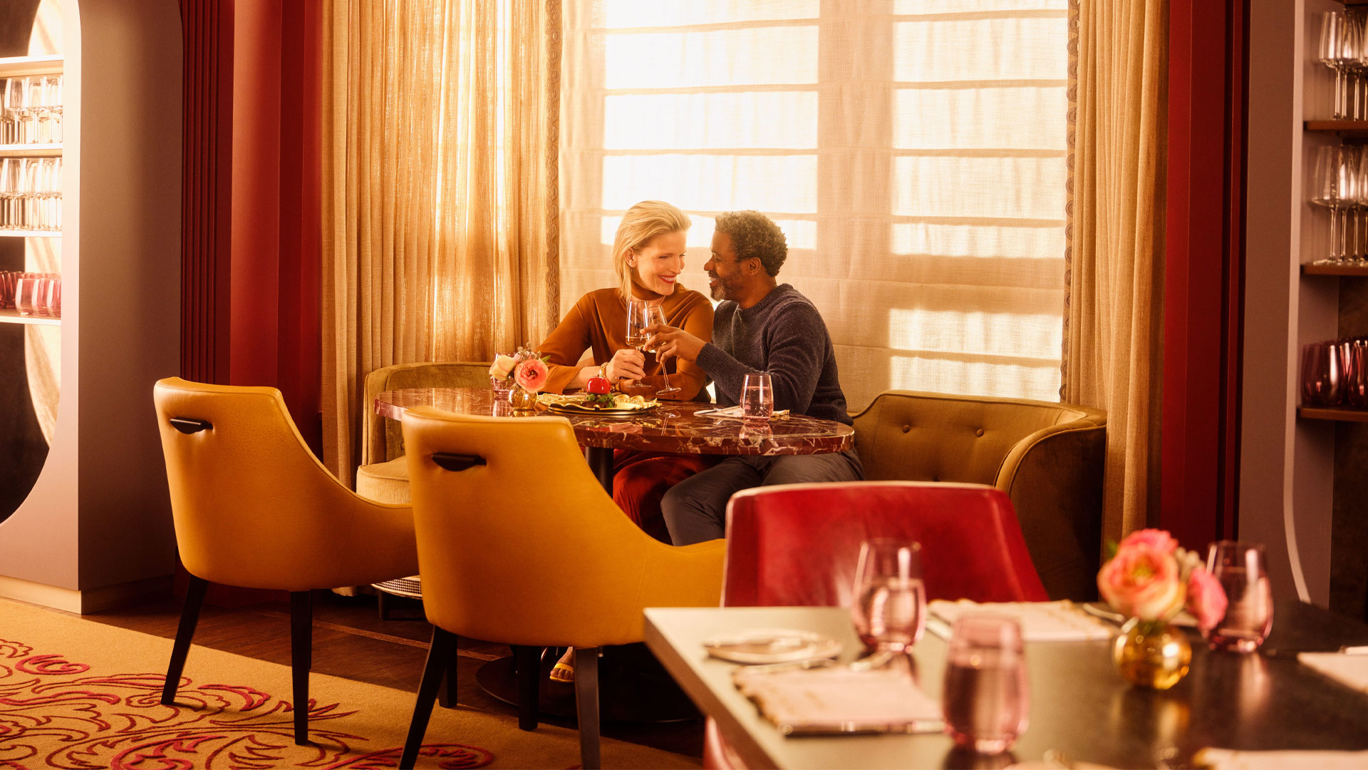 Couple seated in a booth sharing a meal in front of sunlit windows.