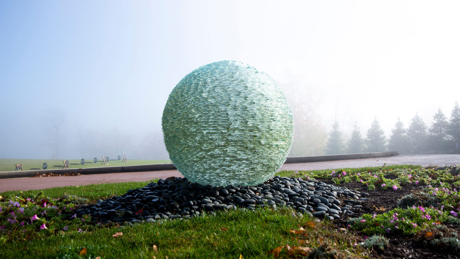 Glass ball sculpture on a grass field on a misty day with trees in the background.