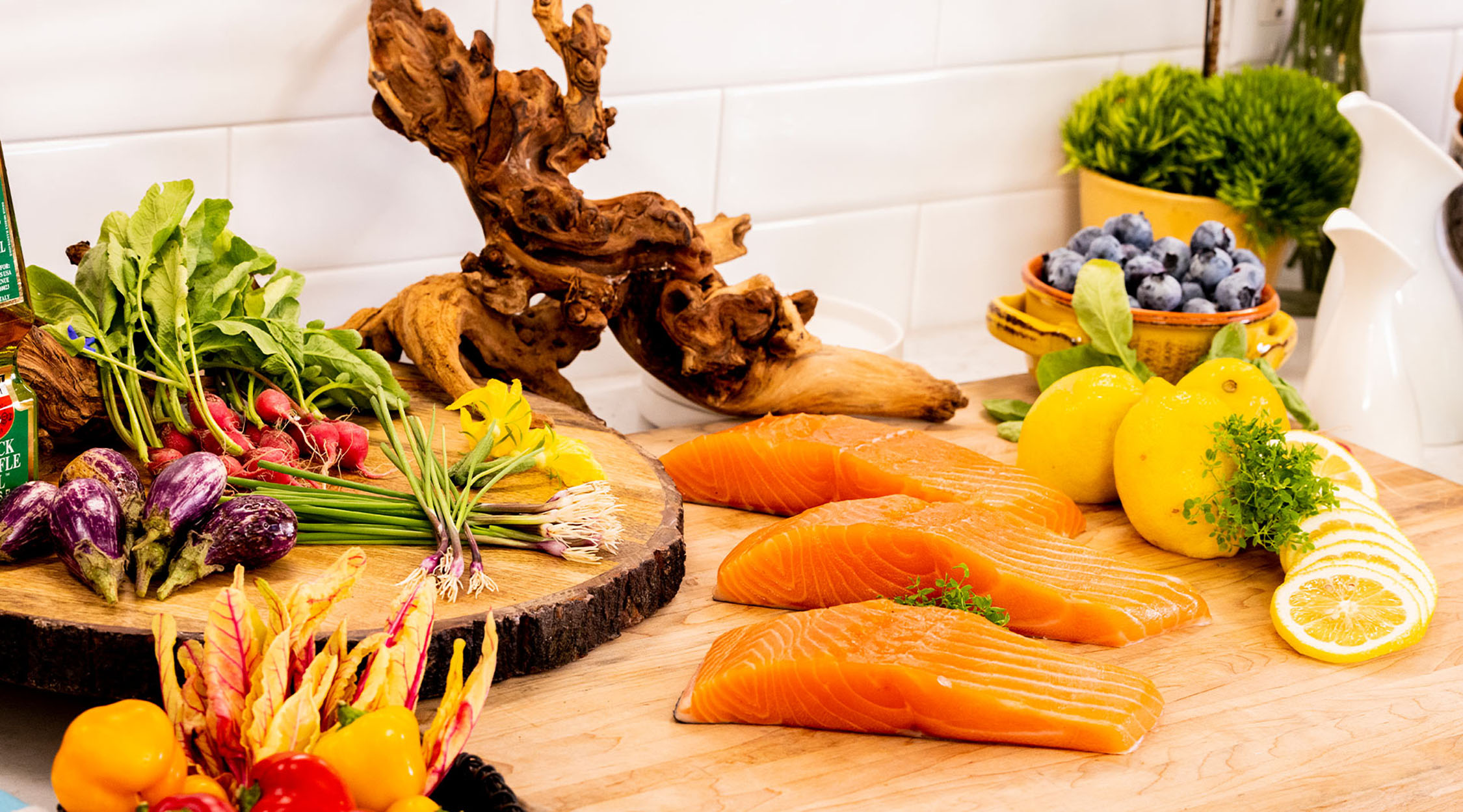 A colorful wooden board showcasing slabs of salmon, vegetables and greens with a large root in the background