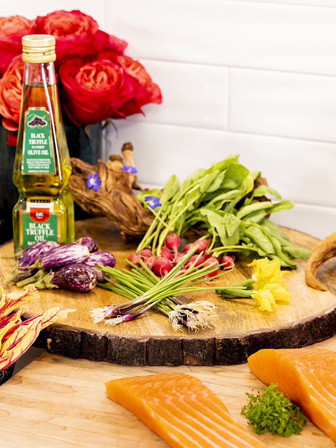 Greens, vegetables, and truffle oil displayed on a wooden disc platter