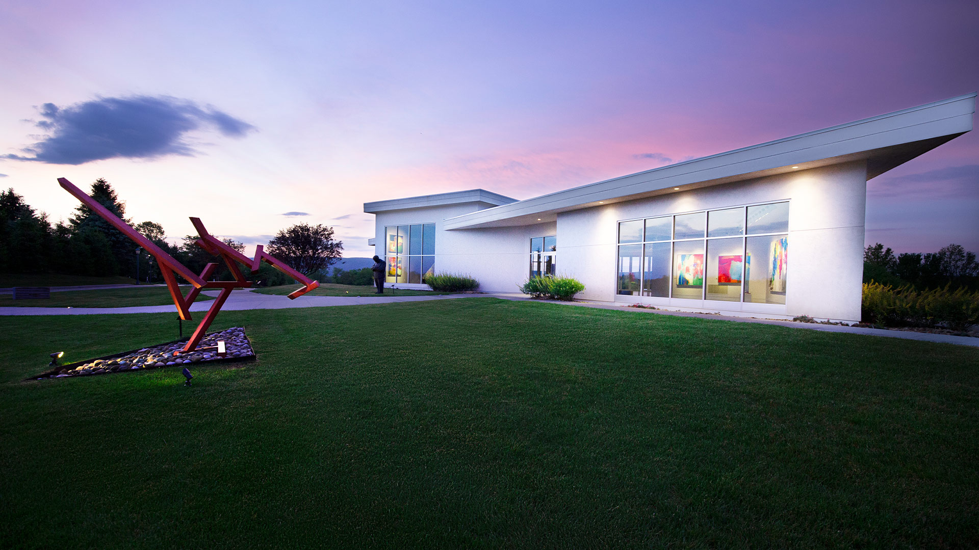 White building at dusk with pink sunset and sprawling green lawn.
