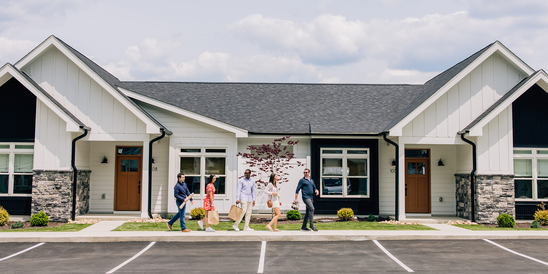 Five people walking on a sidewalk holding groceries and beer