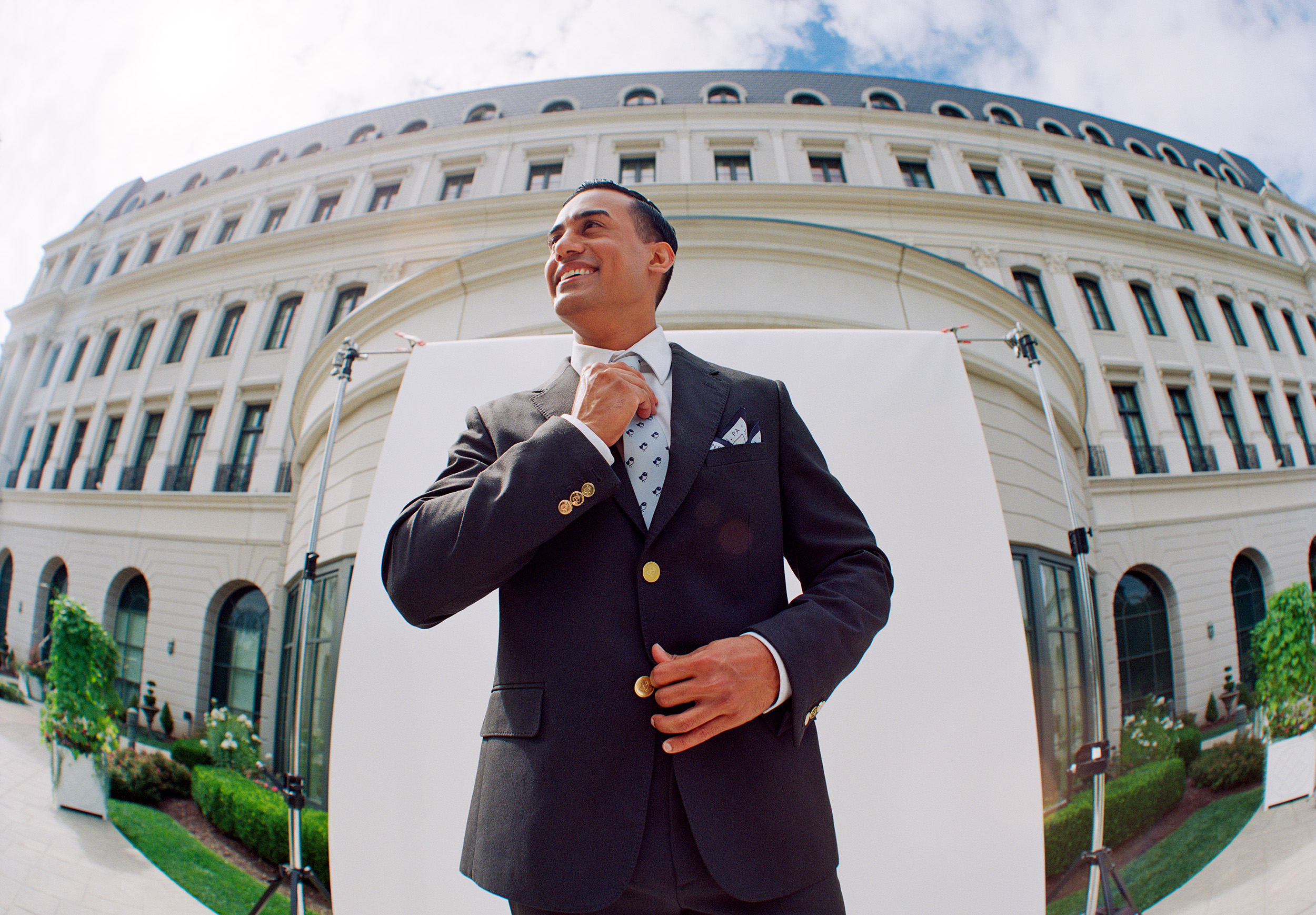 Man in a suit and tie in front of a white hotel